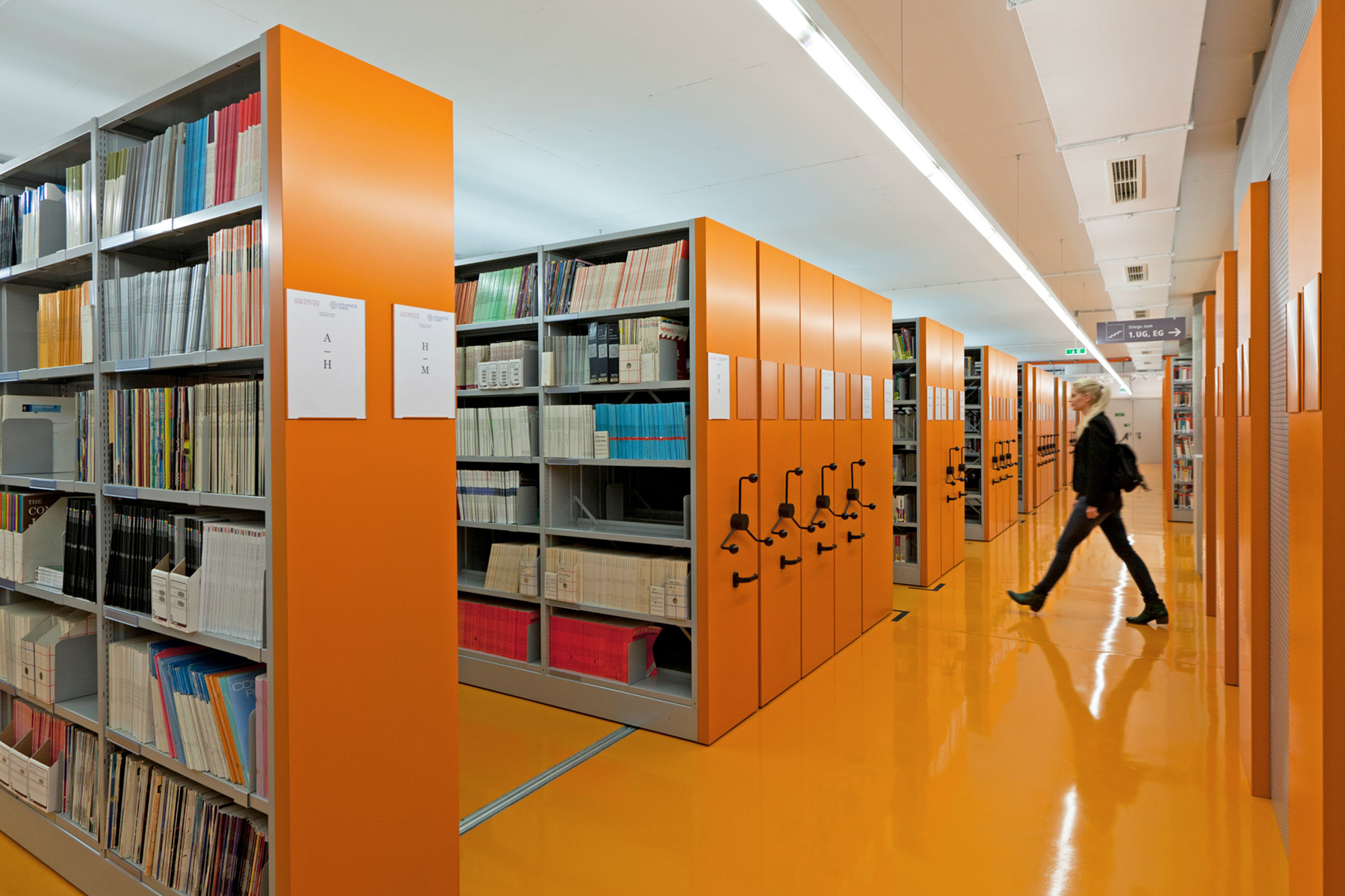 Rollregale in einer Bibliothek mit orangen Vorsatzwänden, passend zum orangen Boden des Raumes